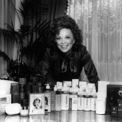 Paula Kent, em preto e branco, na frente dos produtos Redken.